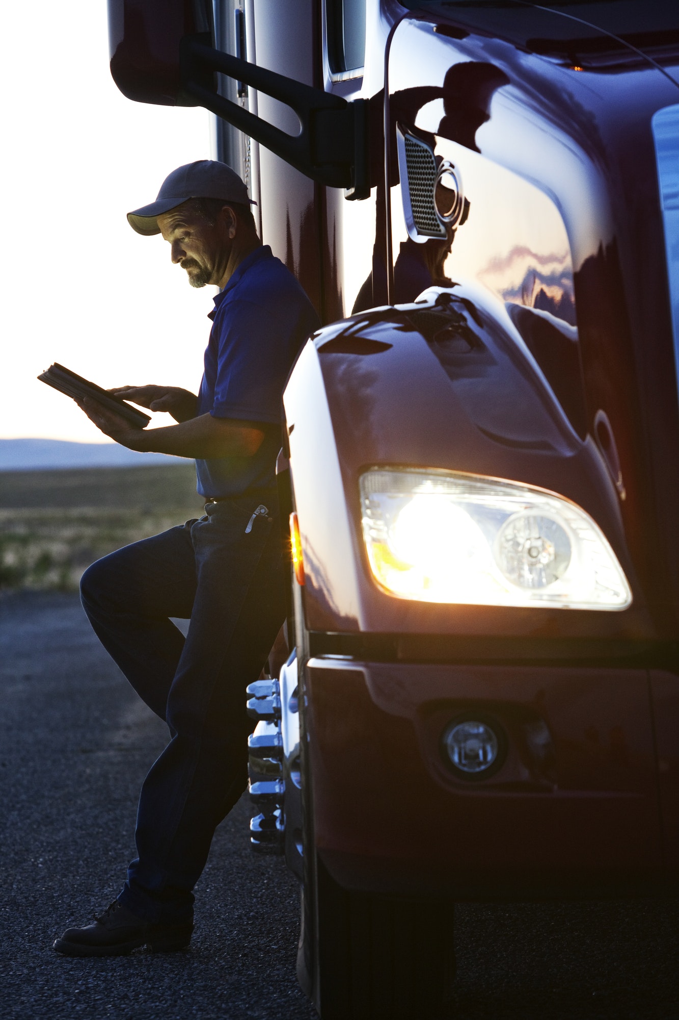 Truck driver checking his notebook computer log while standing next to the cab of his commercial